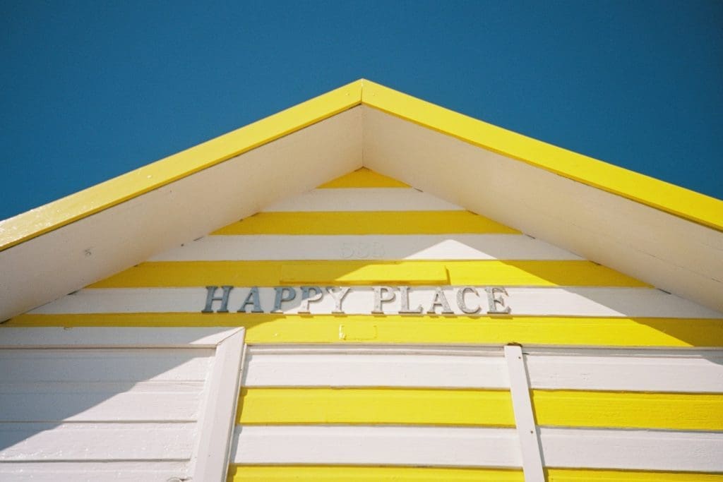 a yellow and white stripped beach hut with happy place on it