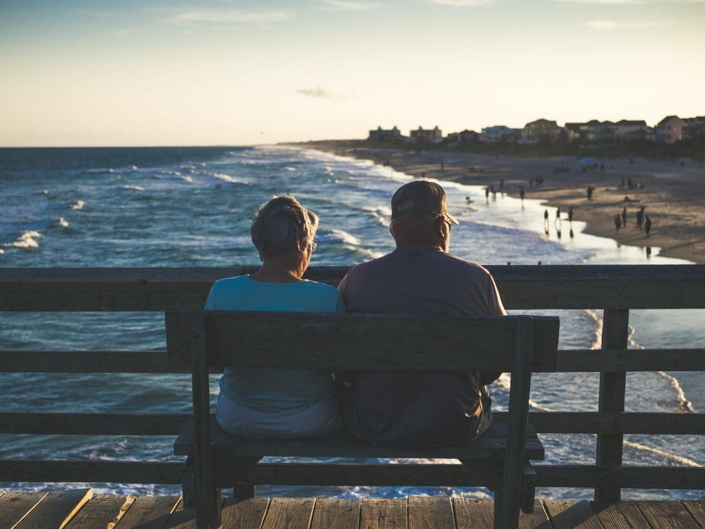 elderly couple sat on a bench looking at the sea