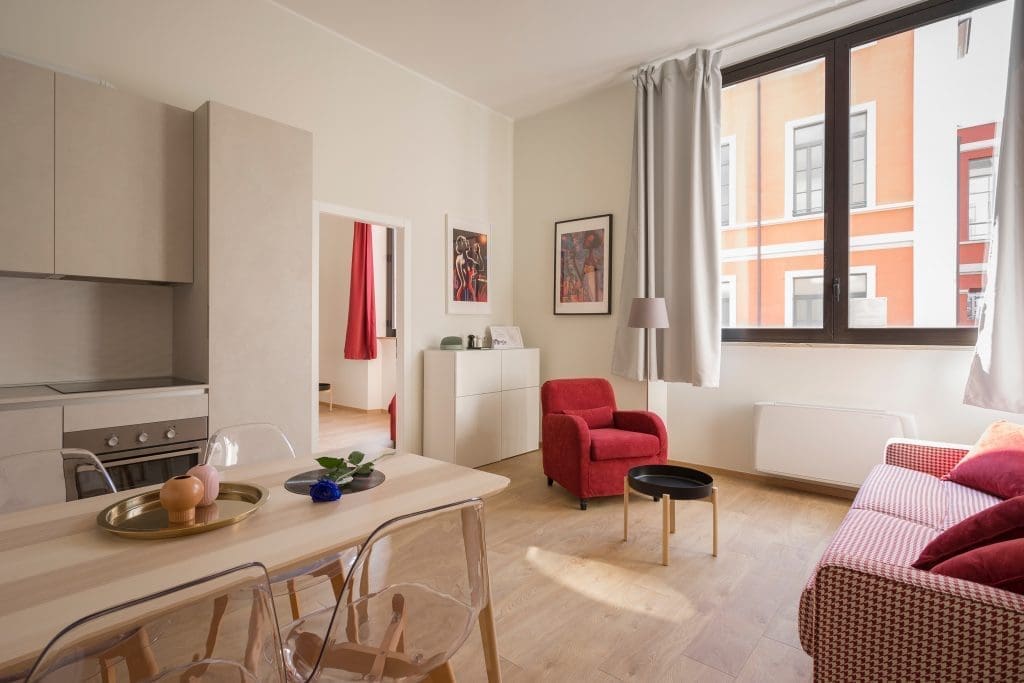 Part Exchanging Homes | Image of a studio apartment with a Red Armchair, Red Checkered Sofa, Dining Table and kitchen with a view of the bedroom