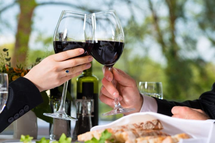 two glasses filled with red wine toasting at dinner table